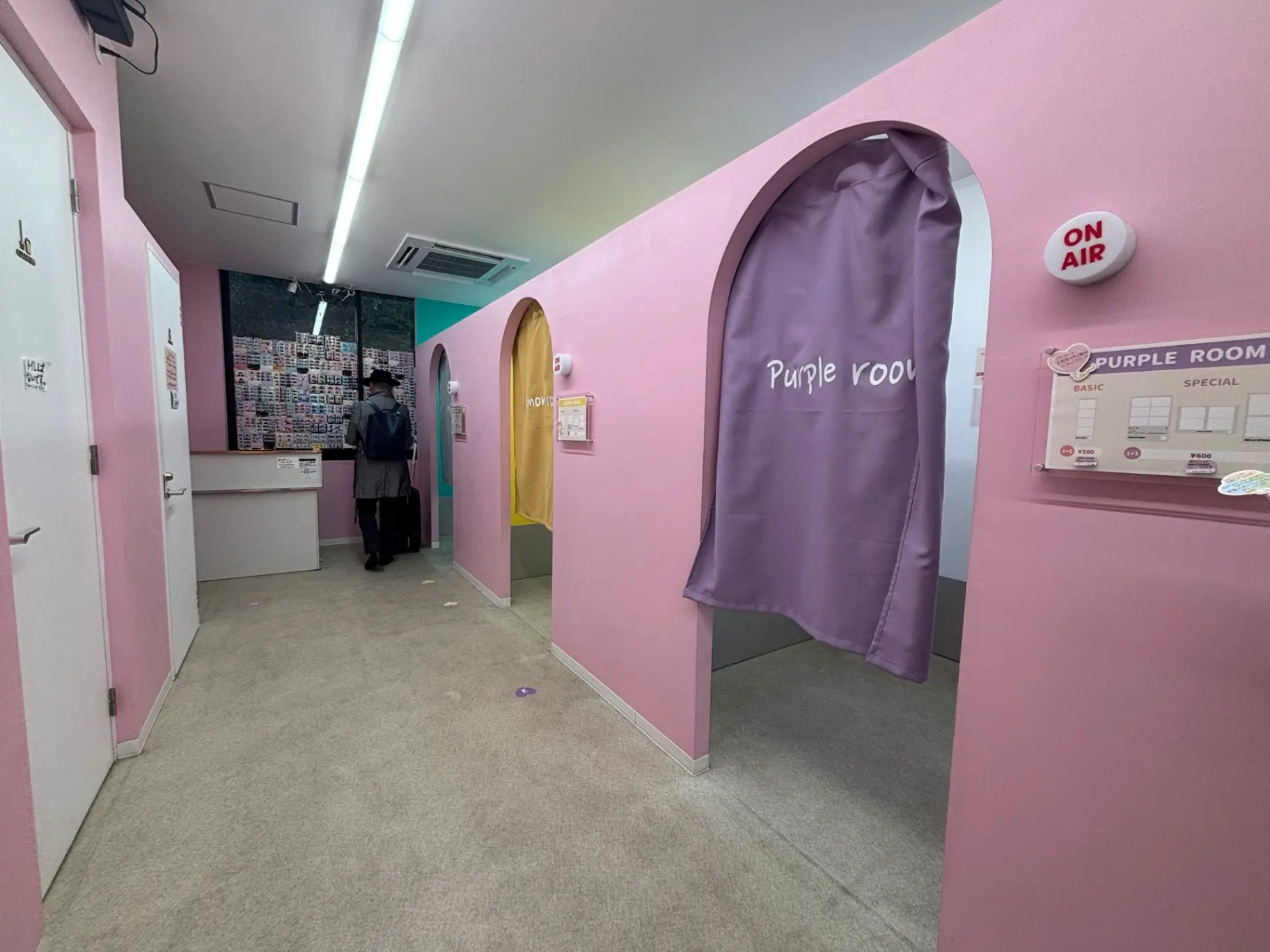 - ピンクの壁に囲まれた廊下、アーチ型の入り口と「Purple room」のカーテン、受付カウンターで何かを見ている人物のシーン