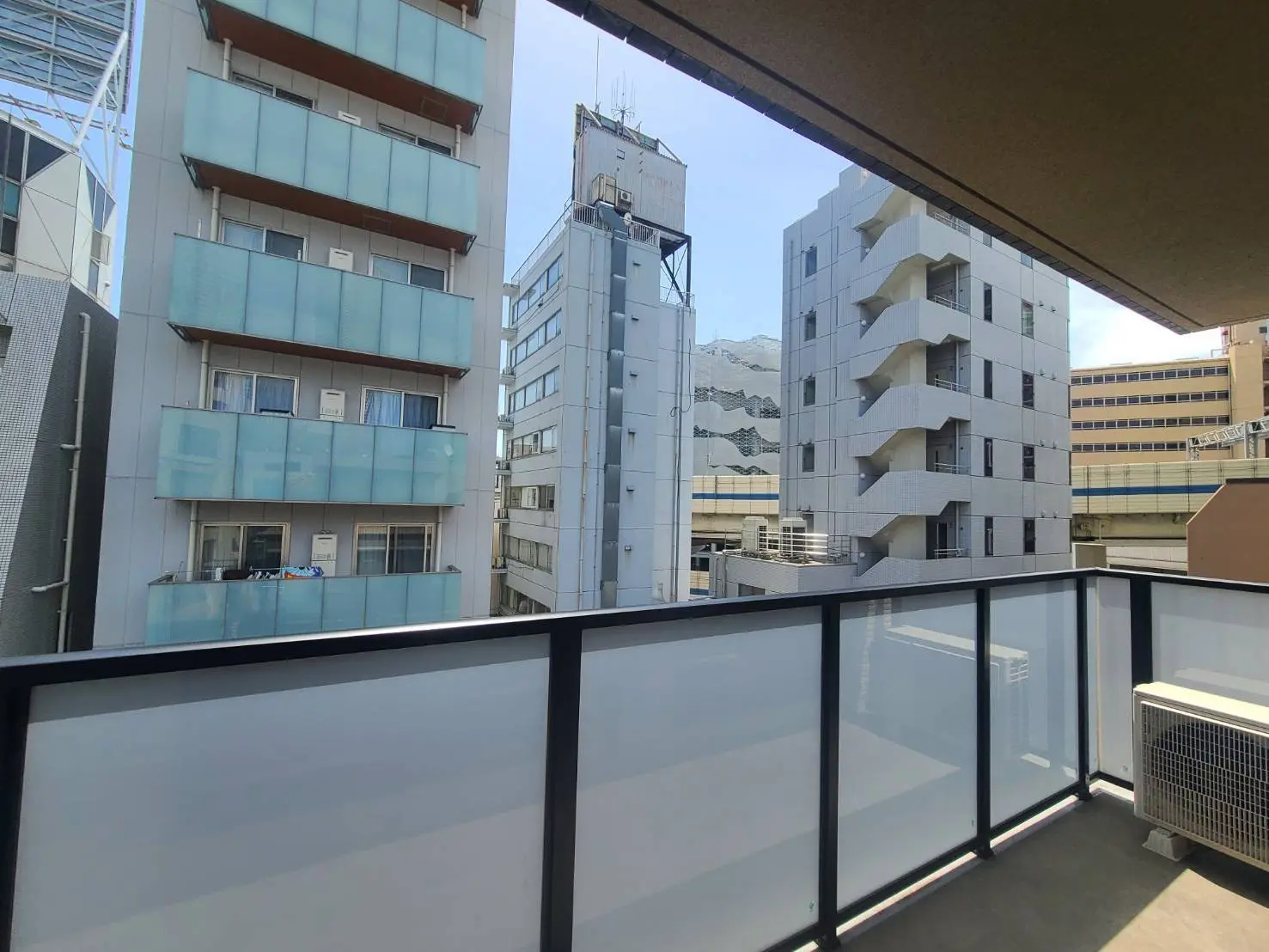 - 都市のバルコニーから見える高層ビル群、ガラスの手すりと青空が印象的な景色