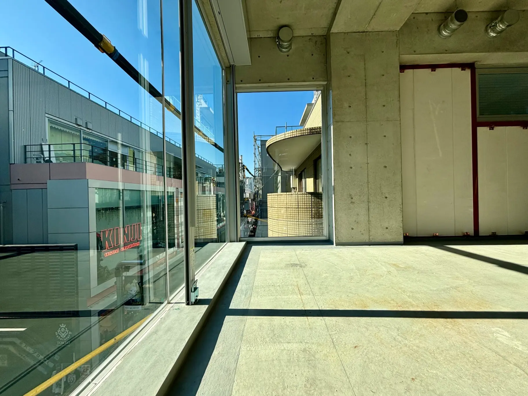 - 大きな窓から明るい日差しが入るコンクリート壁の室内、外の建物が見える風景