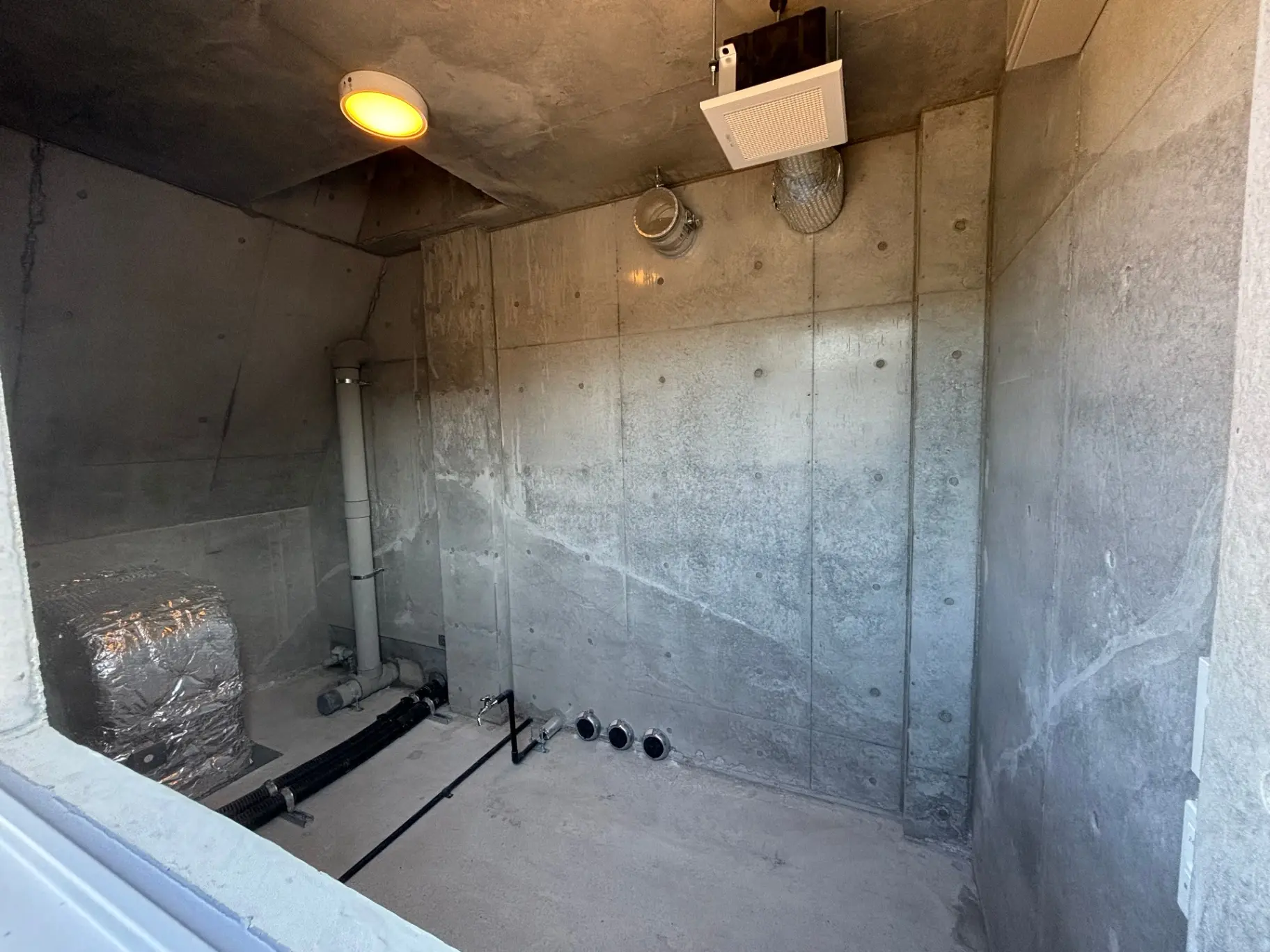 - コンクリート製の無機質な空間、照明が設置された屋内の作業スペース、配管やダクトが見える構造デザイン