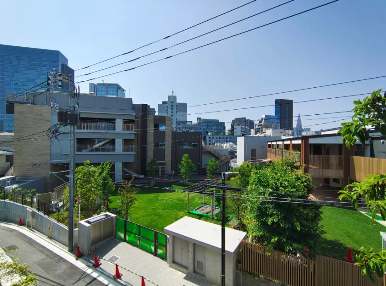 - 都市の景観を背景にした広々とした緑地、近代的な建物と芝生、青空の下に電線が走る風景