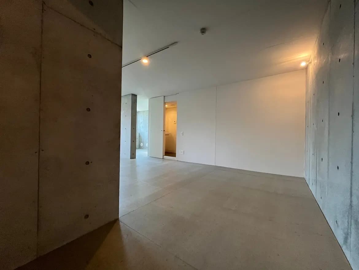 - コンクリートの壁と床が特徴的な広々とした居住空間、明るい照明とシンプルな内装が印象的なインテリア