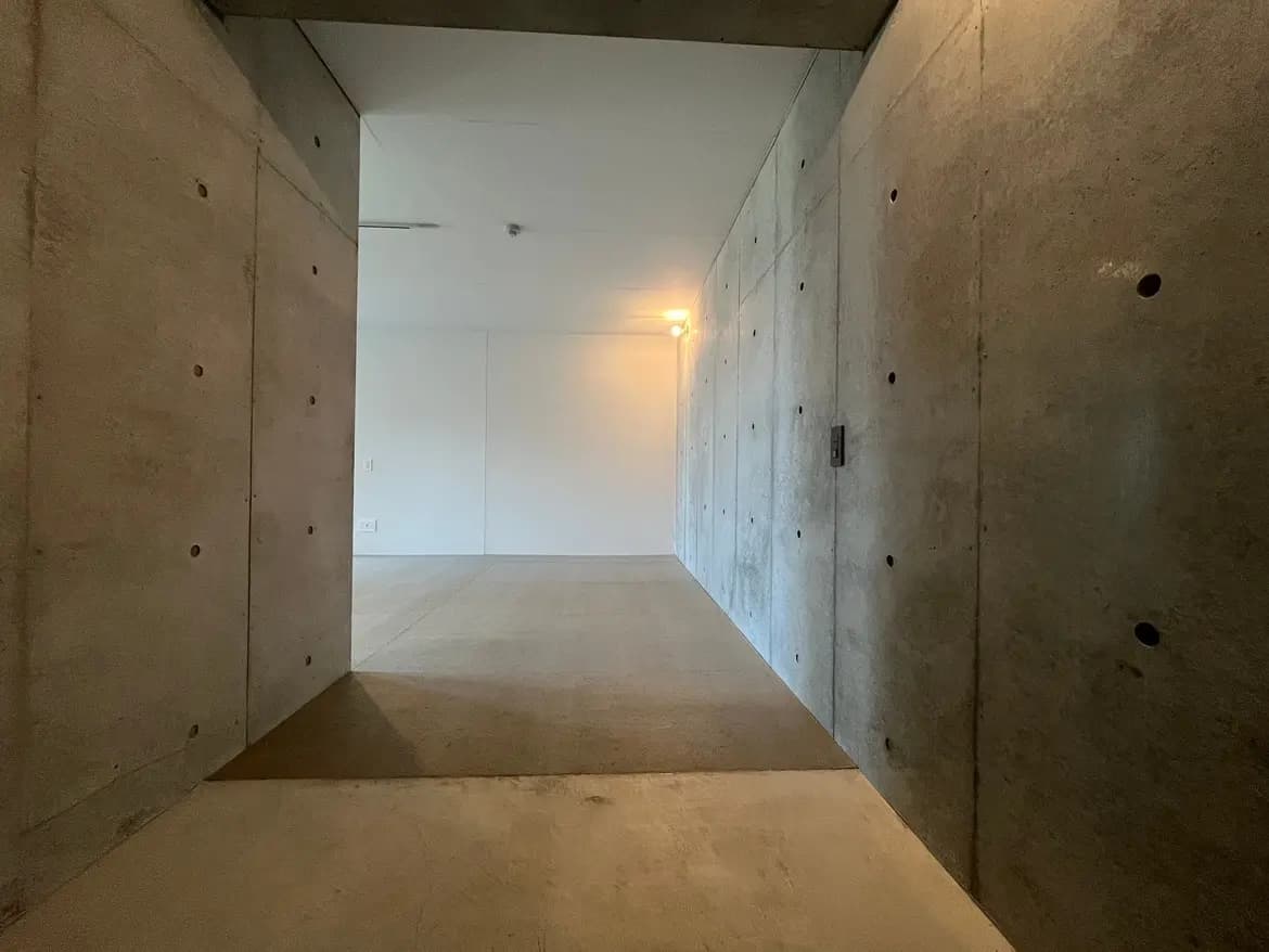 - コンクリートの壁で構成されたモダンなエントランス、明るい照明が特徴のシンプルな室内空間