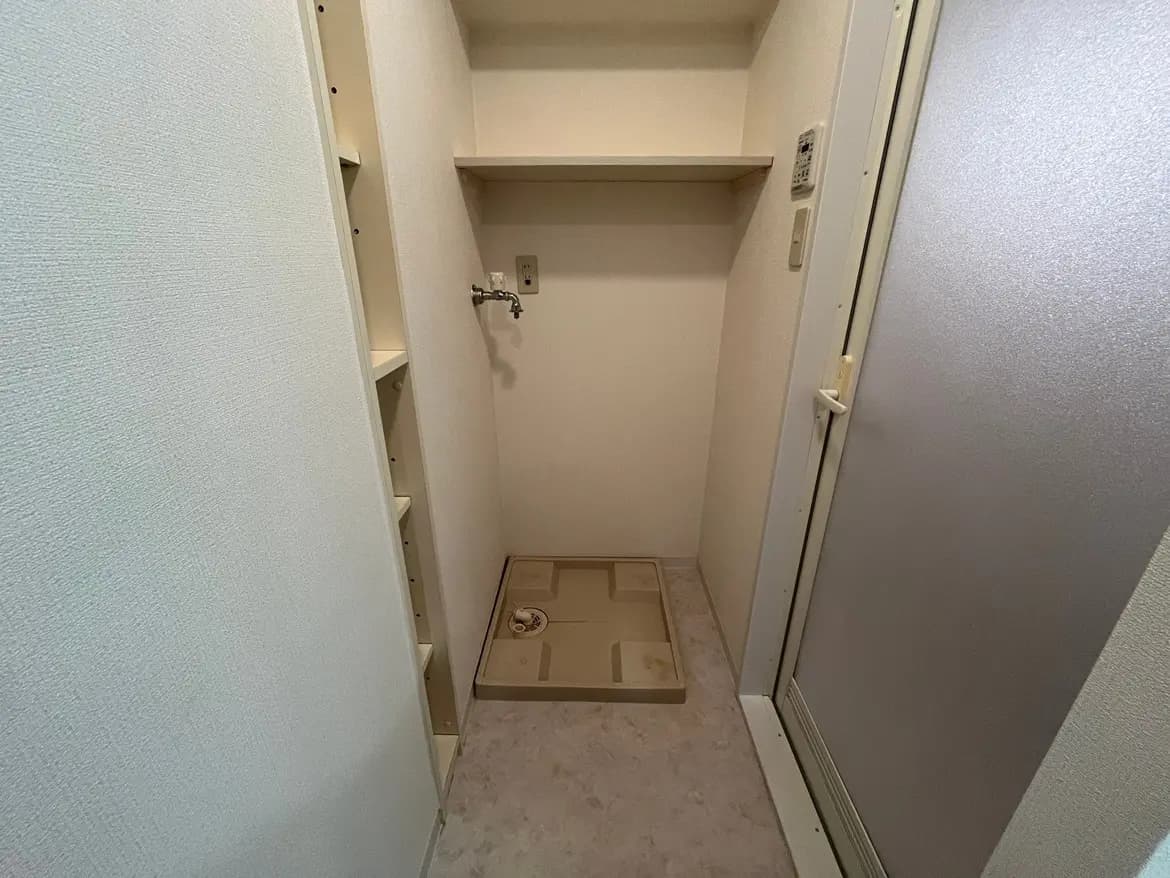 - 清潔感のある洗濯機置き場、壁面に収納棚、混合水栓と排水口がある空間
