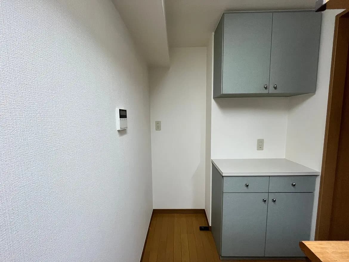 - シンプルなデザインの収納キャビネットと壁の温度調節パネルがある白い空間の内部画像
