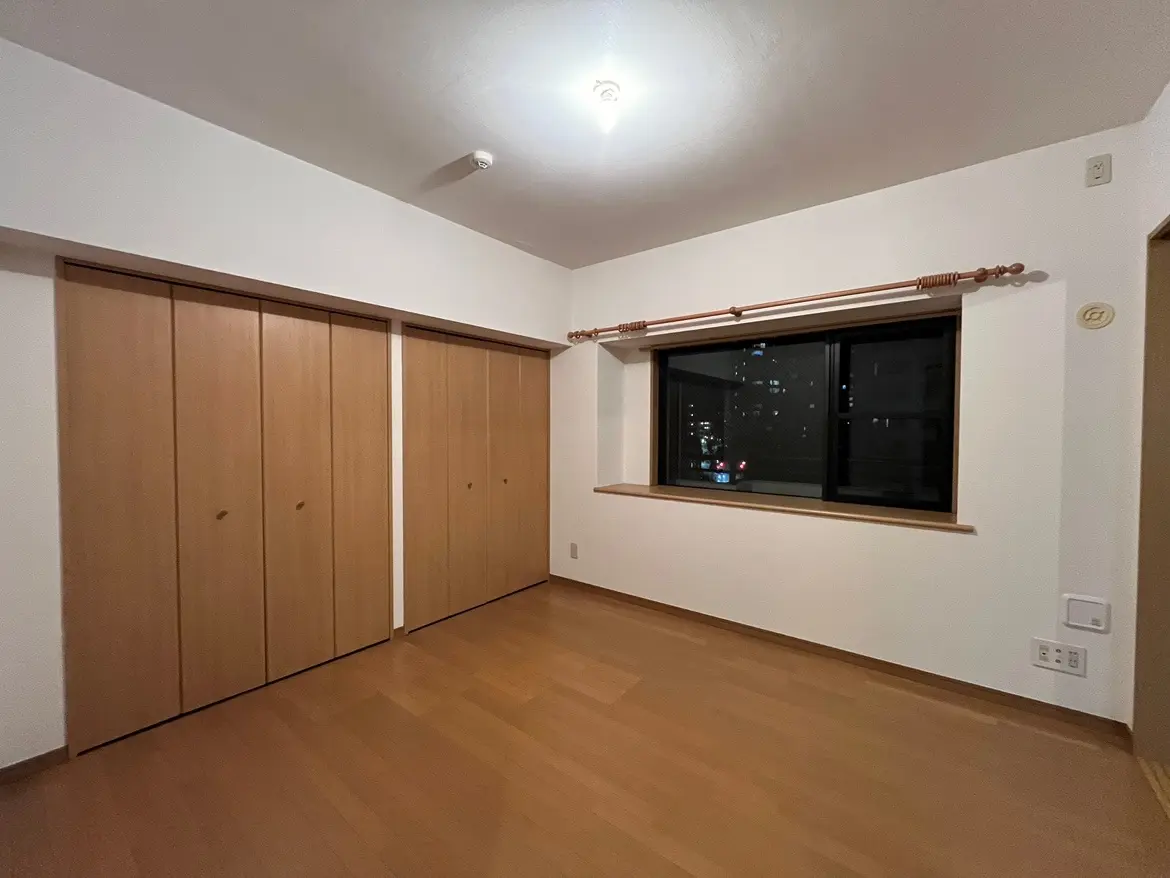 - シンプルで落ち着いた雰囲気の部屋、木製のクローゼットと大きな窓から街の明かりが見えるインテリア