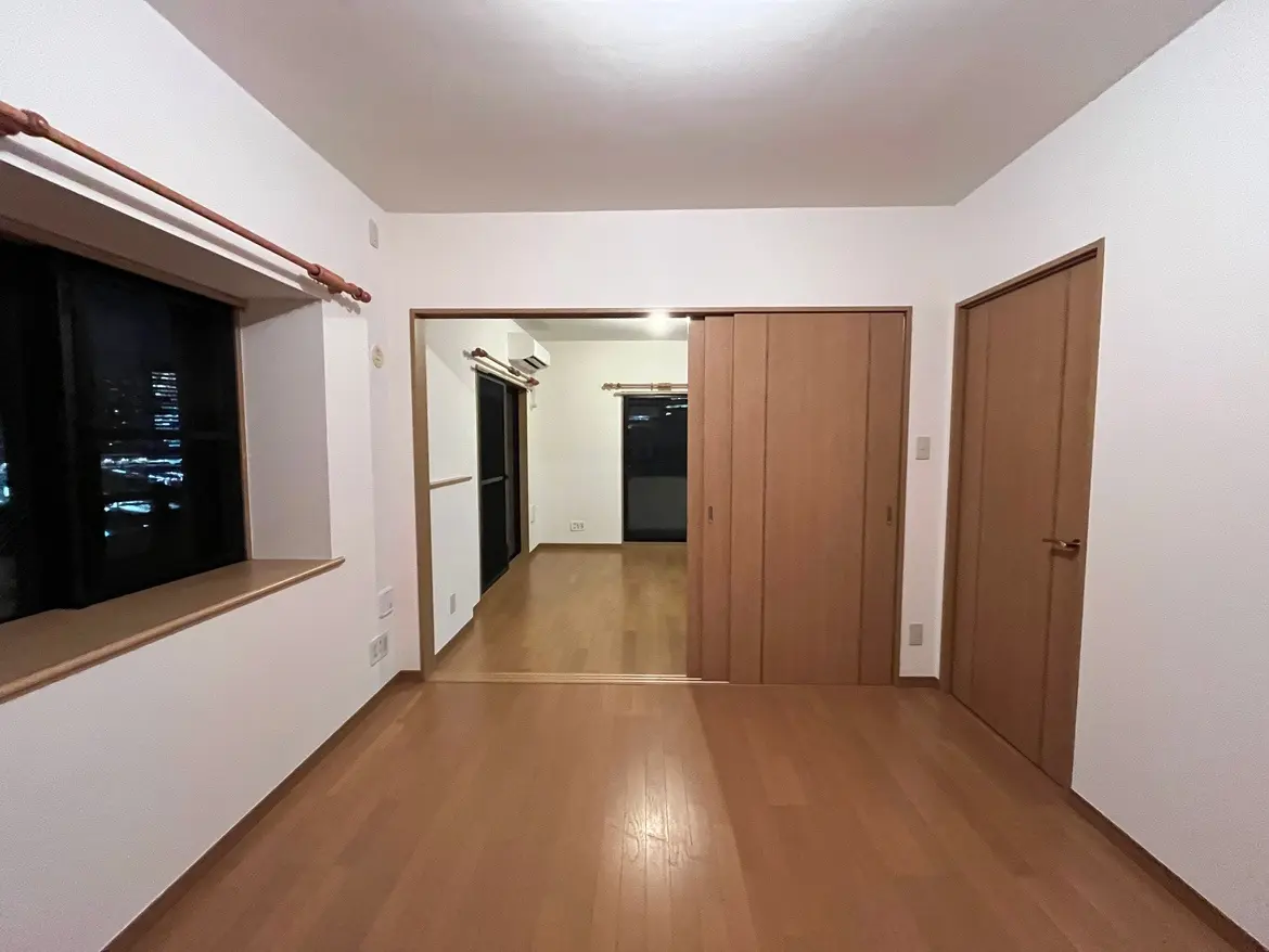 - シンプルなデザインのリビングルーム、木製の床と大きな窓、隣接する部屋への扉がある明るい空間
