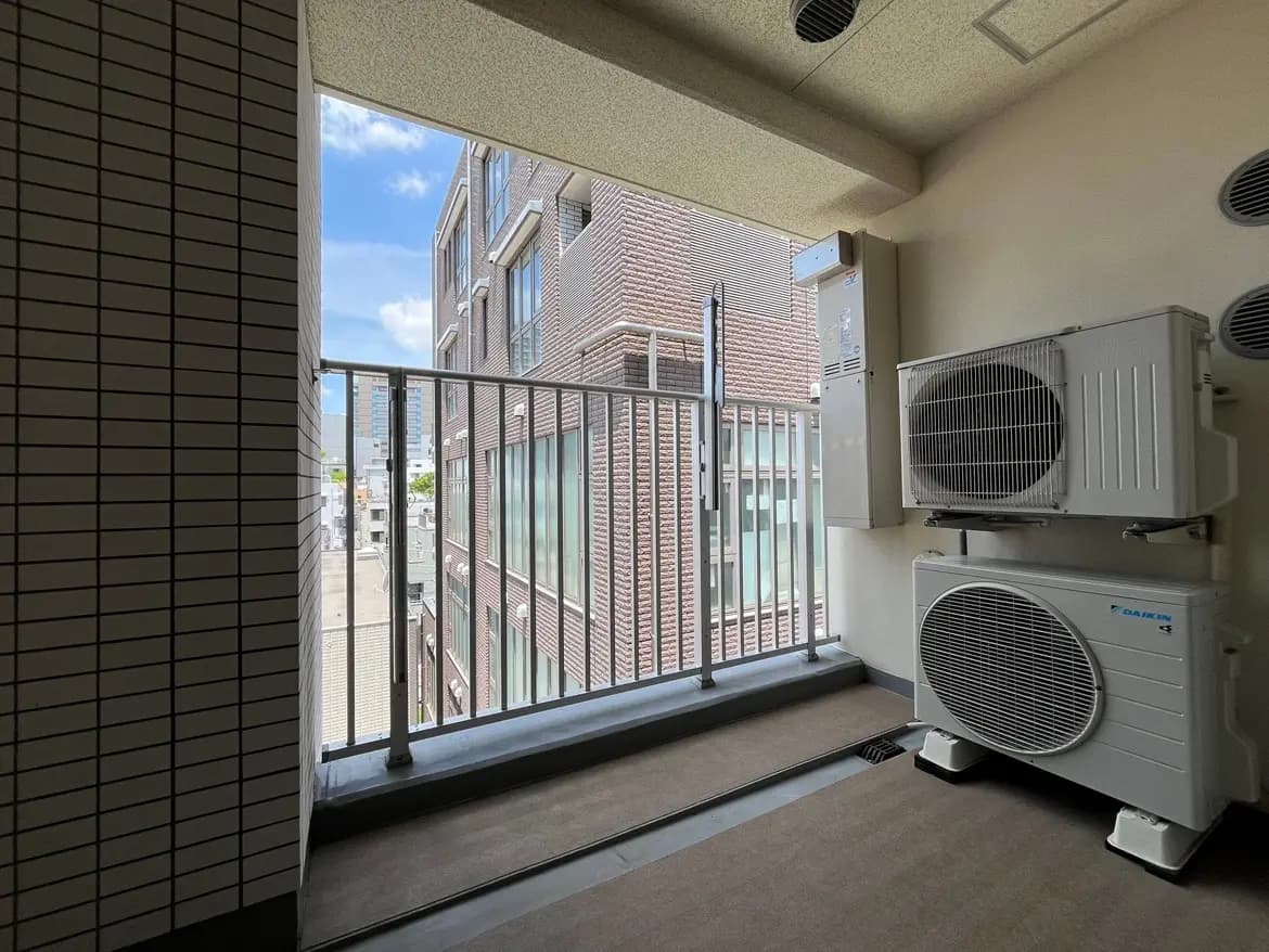 - バルコニーからの眺め、隣接する建物が見える都市の景観とエアコンの室外機が設置された室内の様子