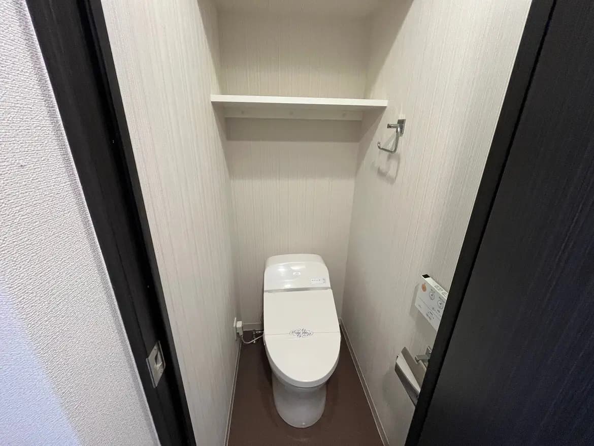 - シンプルで清潔感のあるトイレ、モダンなウォシュレット付き便器とシェルフ、落ち着いた色合いの壁面インテリア