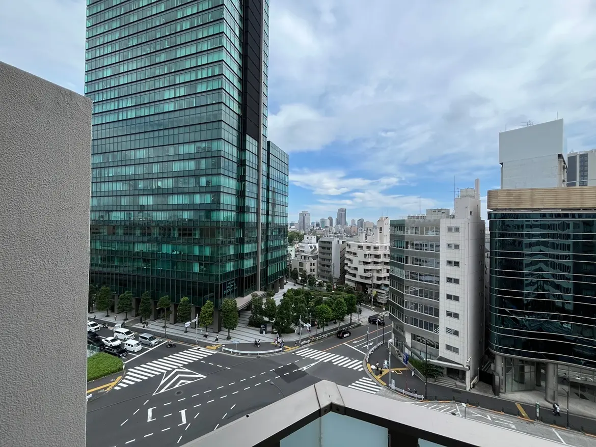 - 都市の景色を望むバルコニーからの眺め、摩天楼のビル群と青空、交差点に車と人々が見える風景