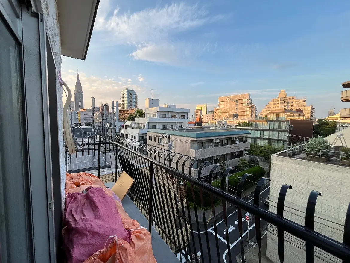 - ベランダから見える東京の街並み、遠くに東京タワーやビル群が広がり、夕暮れの柔らかな光が当たる景色