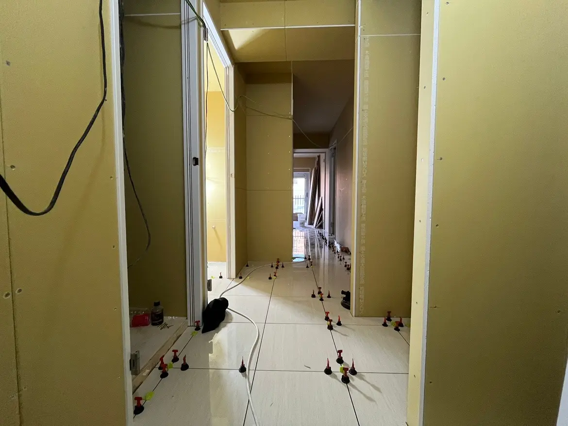 - 新たにタイルが施工されている廊下、薄い黄色の壁、施工中の作業道具やボードが配置されたインテリア