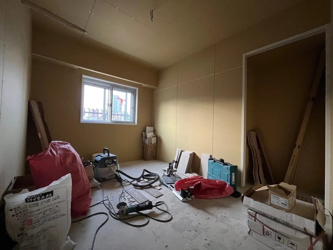 - リフォーム中の空間、黄色い壁と窓がある部屋、作業道具や資材が散らばった様子