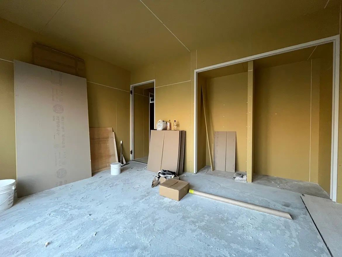 - 工事中の部屋、壁紙がはがれている状態の内装、床に散乱した建材や道具が見える様子