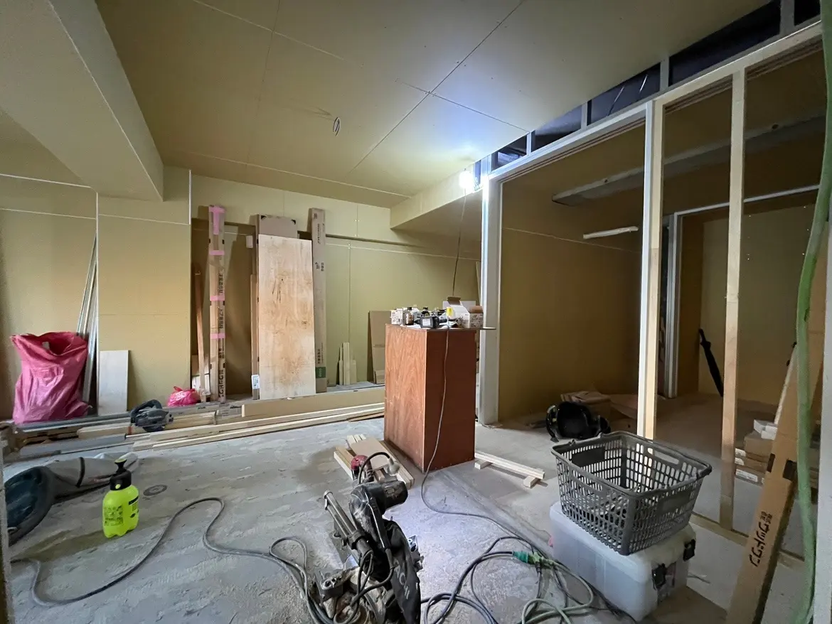- 建設中の室内、壁材と木材が積まれた工事現場の様子、作業工具や収納ボックスが散らばるスペース