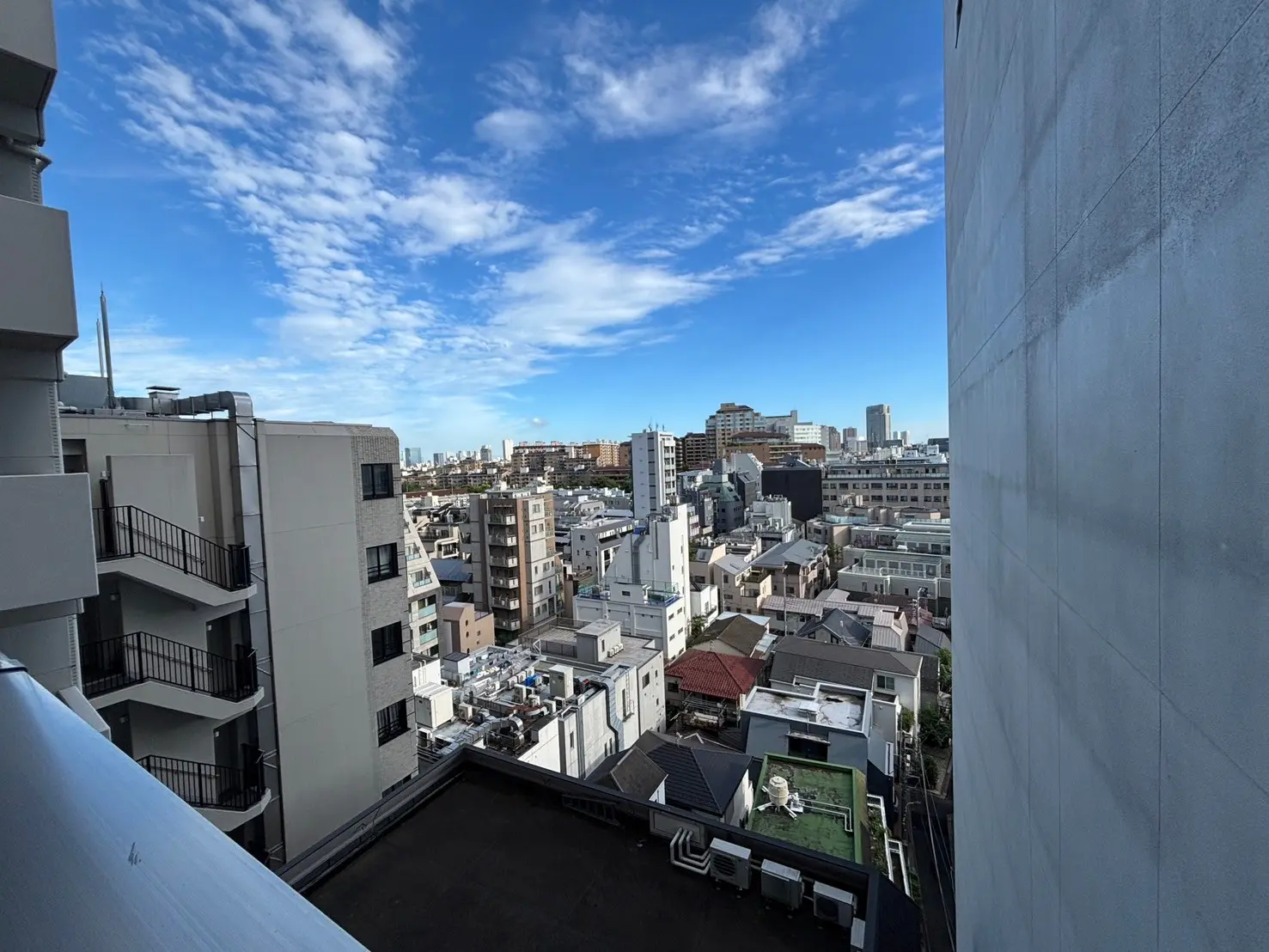 - 都会のビル群と青空の景色、左側に近隣の建物のバルコニーが見える風景