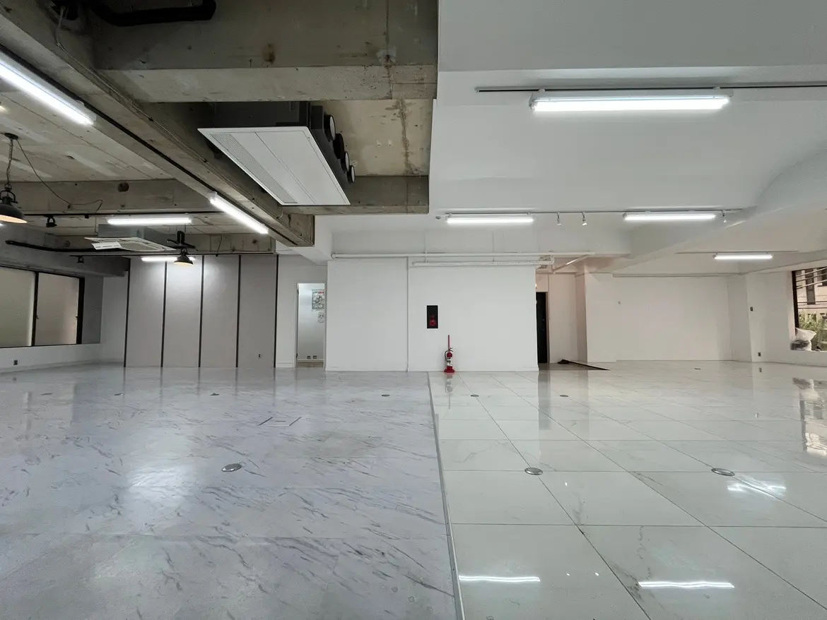 - 広々としたオフィススペース、モダンな照明と白いタイルの床、コンクリート製の天井が特徴的なインテリア