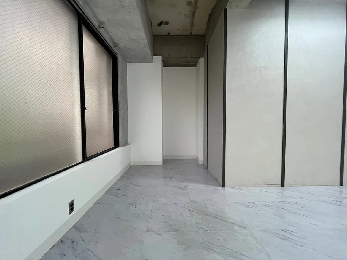 - 大きな窓があるシンプルなインテリアの部屋、コンクリートの天井と流れるような大理石風のフロア、白い壁で仕切られた空間