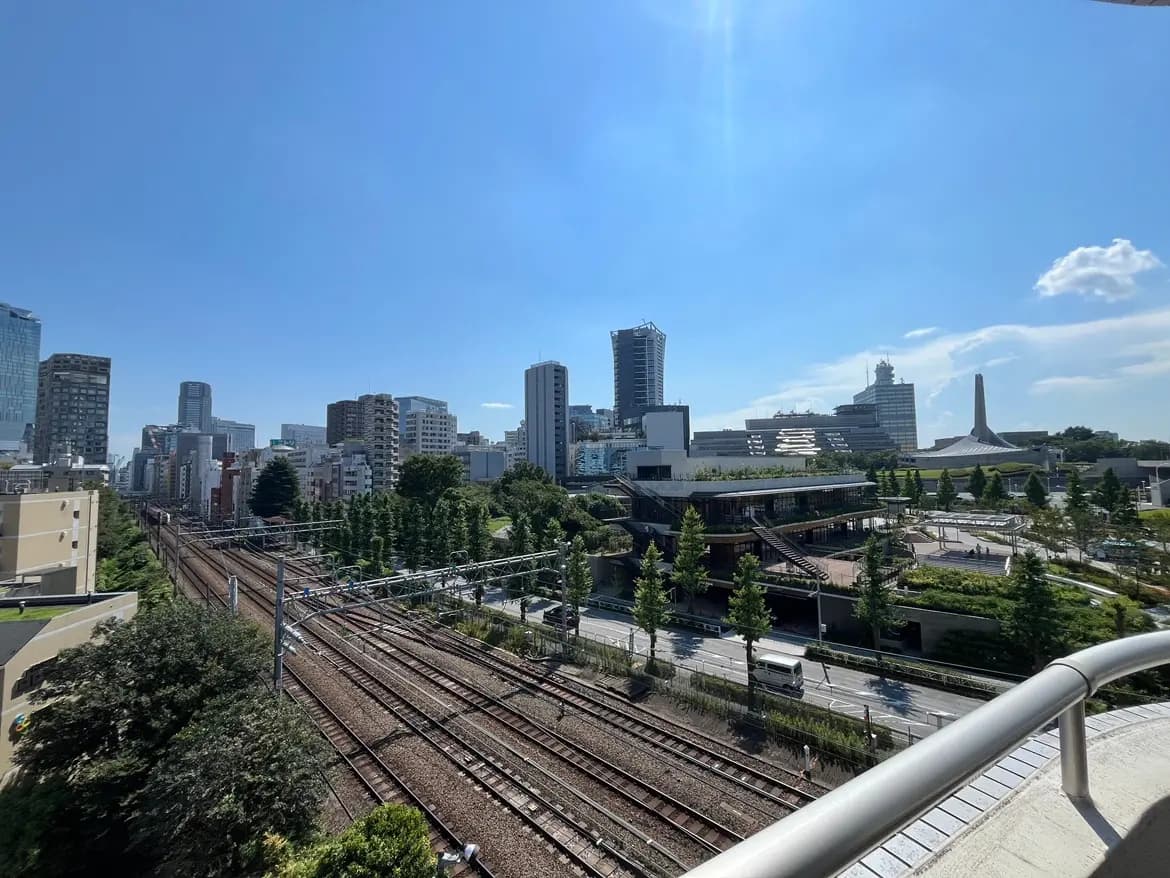 - 青空の下、東京の高層ビル群と鉄道路線が見える風景、緑豊かな樹木と近代的な建物が共存する街並み