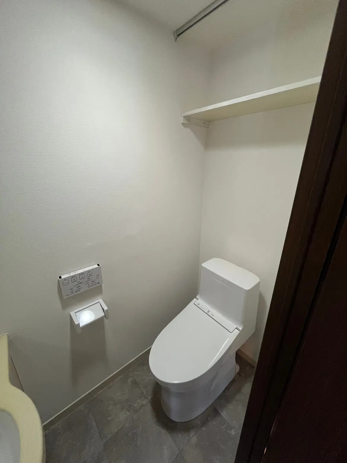 - モダンなトイレの内部、清潔感のある白い壁、シンプルなデザインのウォシュレット付きトイレと収納棚が設置された空間