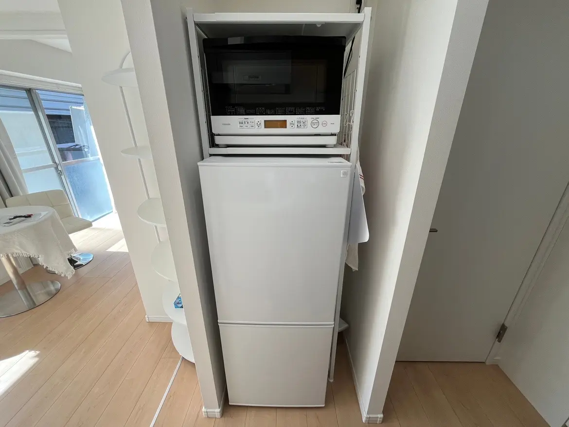 - スタイリッシュなキッチンエリアに配置された白い冷蔵庫と電子レンジ、隣に設置された収納スペースが見えるインテリア