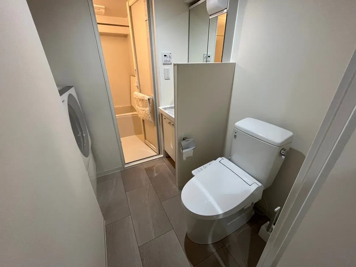 - シンプルで清潔感のあるトイレルーム、白い便器と洗面台、隣に洗濯機とバスルームがあるインテリア