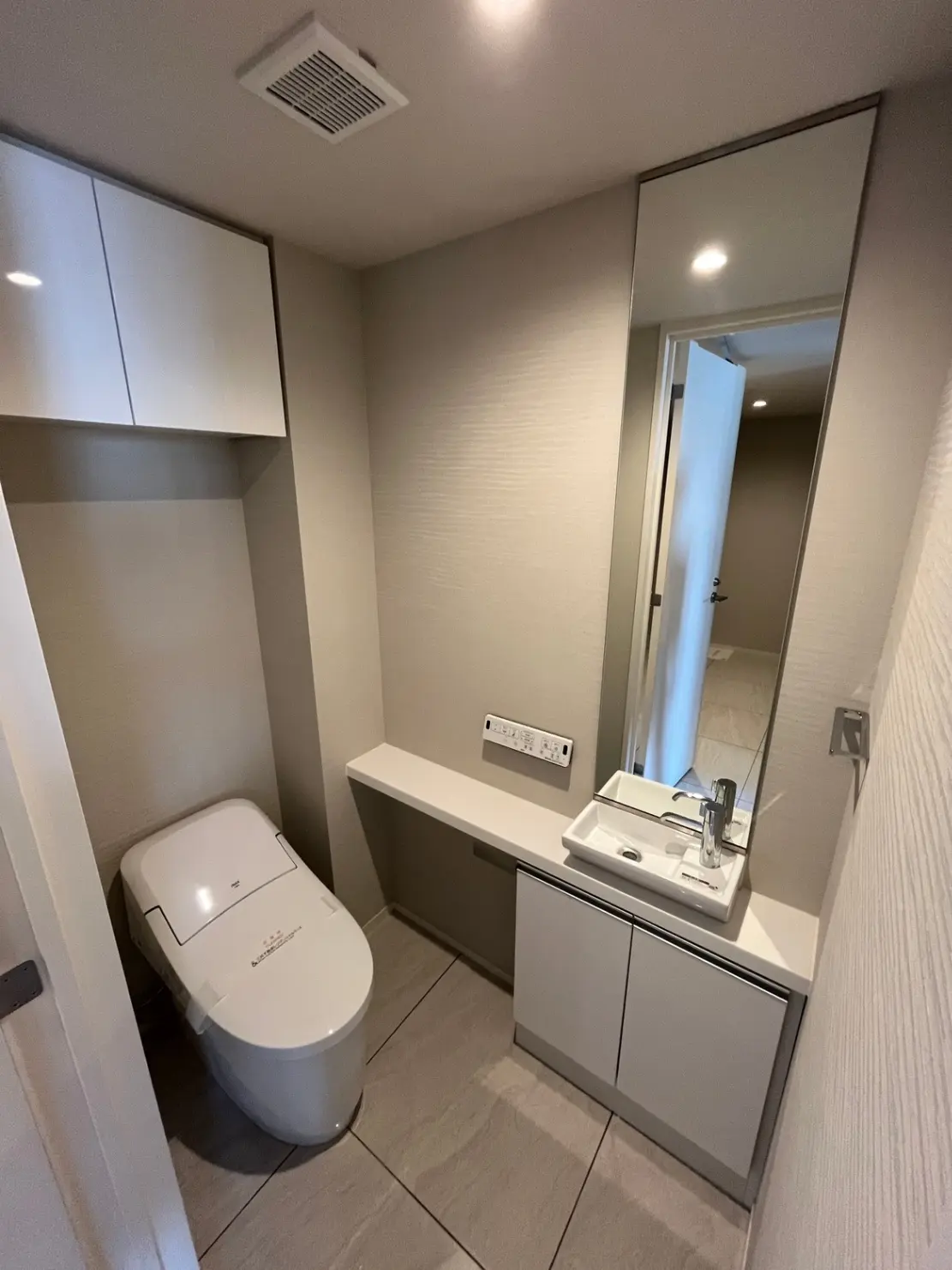 - シンプルでモダンなデザインのトイレ空間、白い便器と洗面台、鏡付きの棚、温かみのある照明が演出されたインテリア