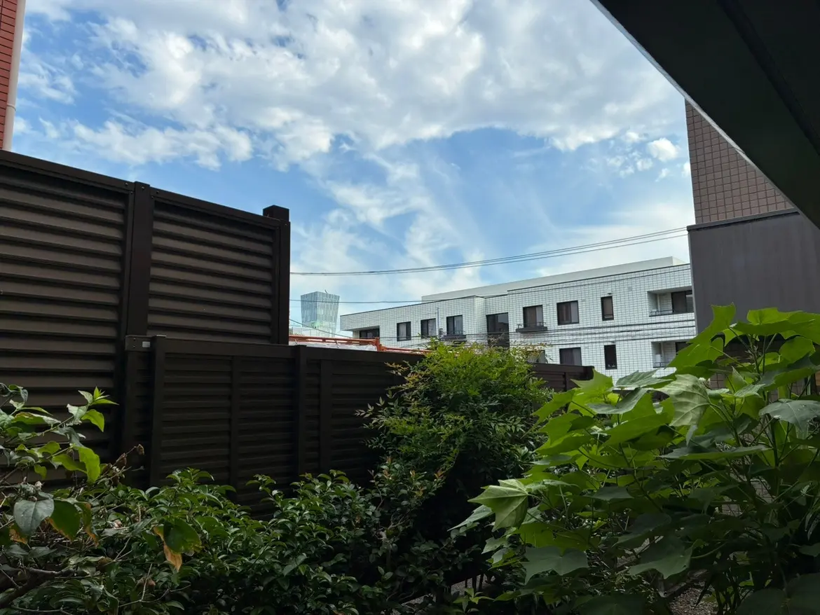 周囲の住宅と緑豊かな庭が見える風景、青い空と白い雲が広がる明るい日中の景色