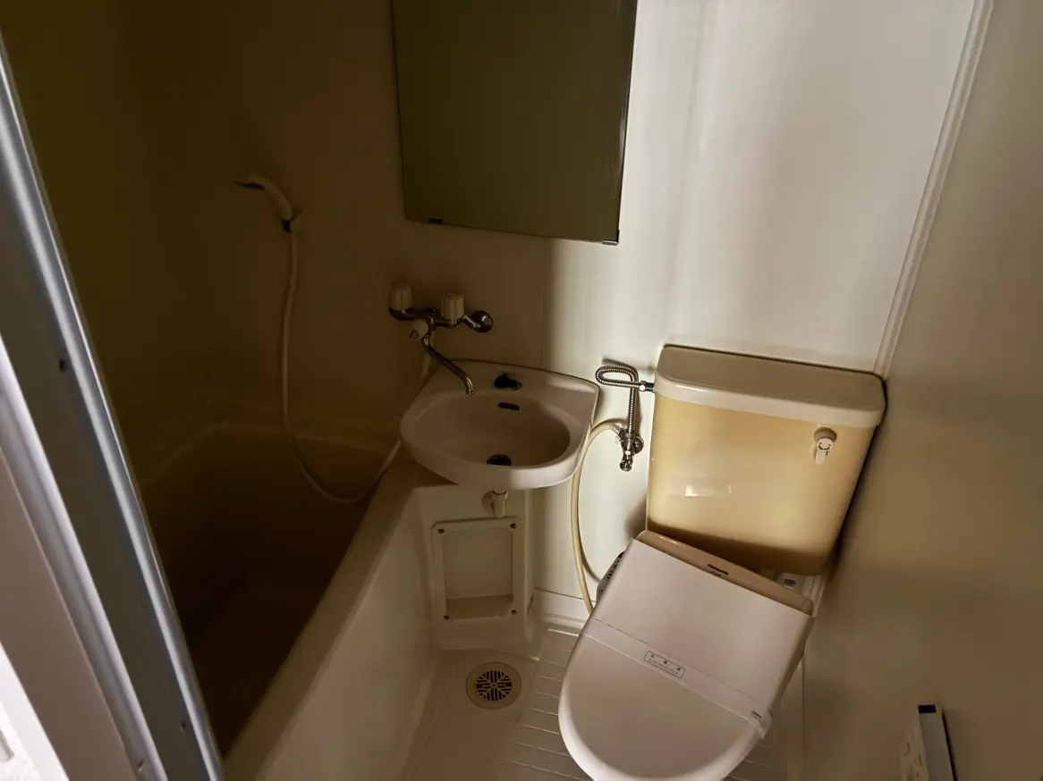 - シンプルなデザインのバスルーム、トイレと洗面台が設置された小スペースで、浴槽とシャワーが一体化した設備