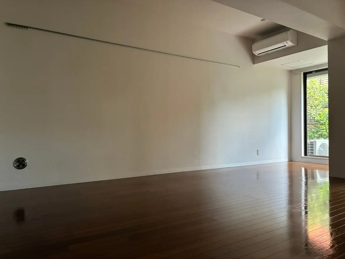 - 白い壁と明るい木製のフローリングのシンプルな部屋、大きな窓から外の緑が見える自然光が入るインテリア
