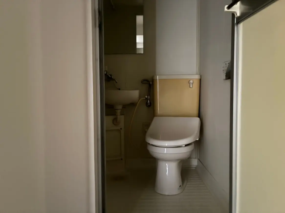 - 明るい洗面所に設置されたトイレと小さな洗面台、シンプルで清潔感のあるインテリア
