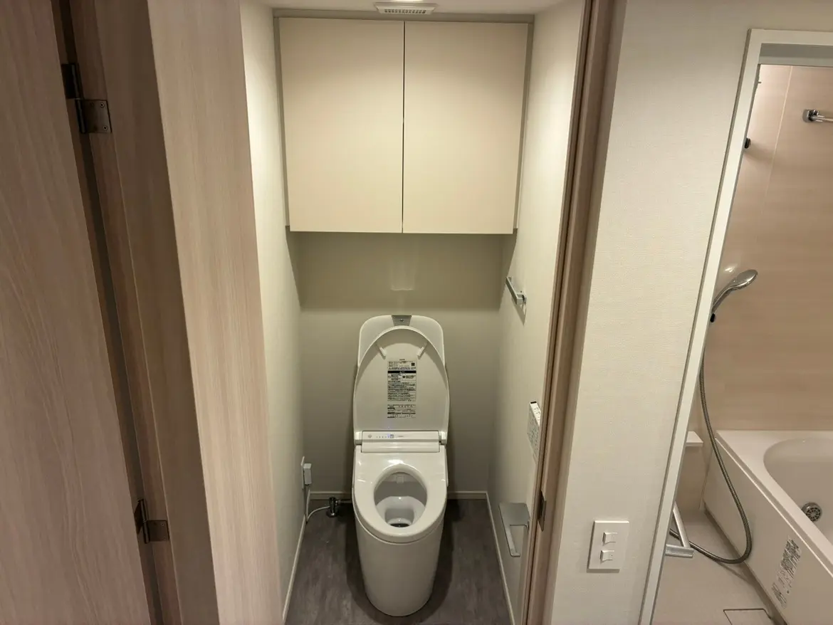 - シンプルで清潔感のあるトイレ室、格納収納付きのキャビネット、最新の洗浄機能付きトイレが配置されたインテリア