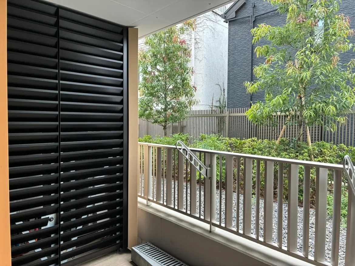 - 黒いシャッターが付いたバルコニー、周囲に植栽された庭と明るい自然光が差し込むスタイリッシュな空間