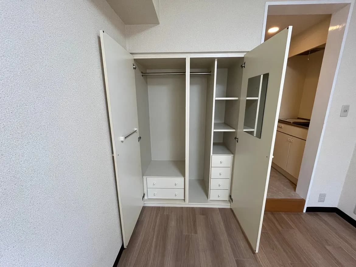 - 扉が開いたクローゼット、棚と引き出しが備わった収納スペース、隣にキッチンが見える部屋のインテリア