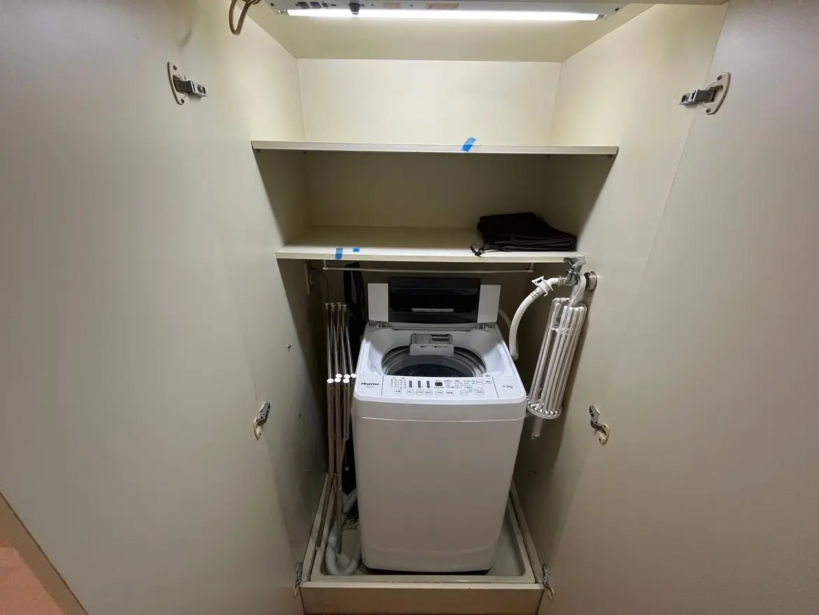 - 家庭用洗濯機が収納された洗濯室、上部に棚がありタオルが置かれているシンプルなデザイン