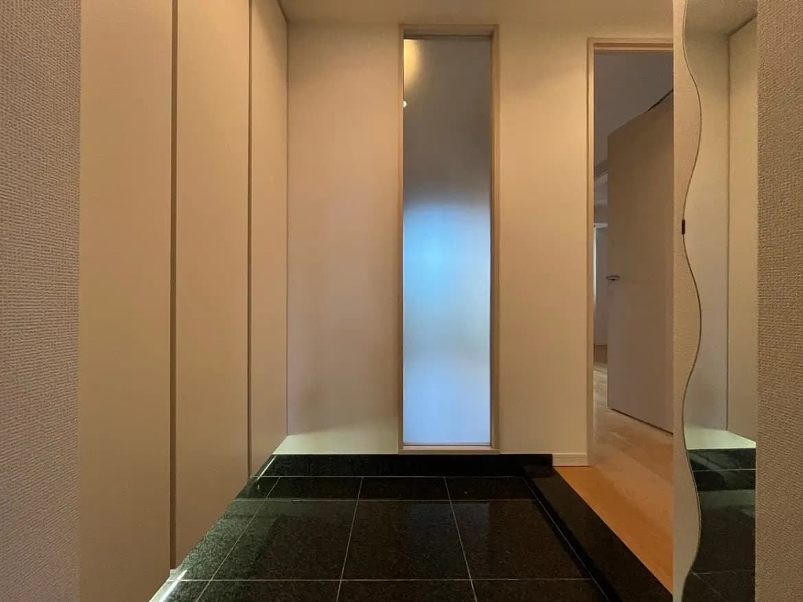 - モダンなデザインのエントランスホール、白い壁と暗いタイルの床、優しい光が差し込む明るい空間