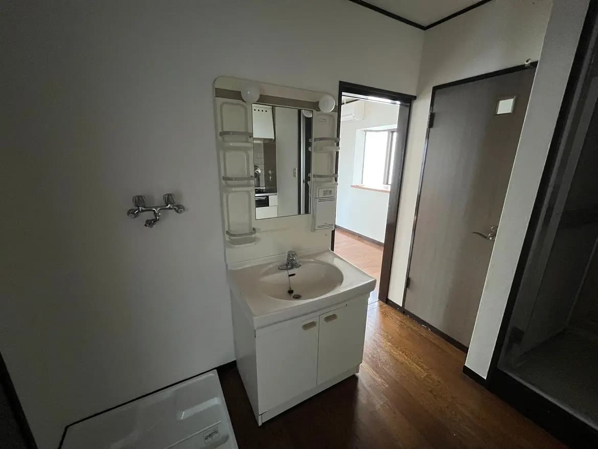 - 明るい洗面所、白い洗面台と鏡、木製フロアが特徴のシンプルな内装