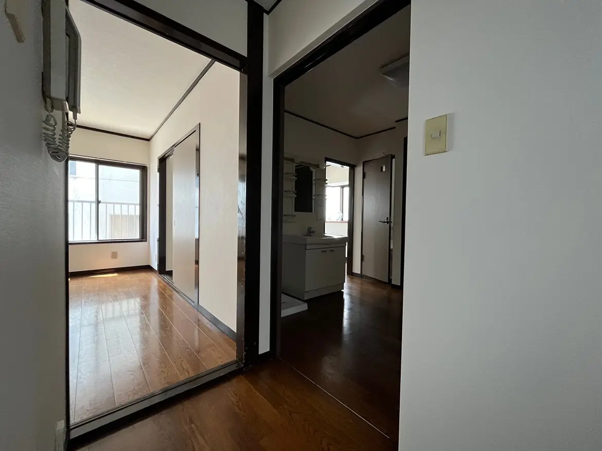 - 明るい色調の廊下、木製フローリングと二つの部屋に続くドア、窓から自然光が差し込む空間