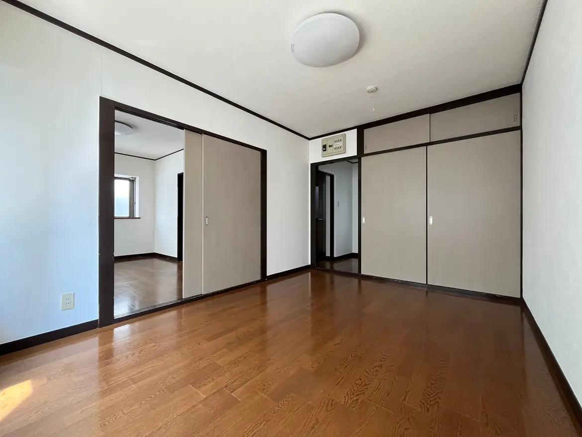 - 明るい色合いの壁と木製のフローリングが特徴のシンプルな寝室、鏡のある収納スペースと自然光が入る窓付きのインテリア