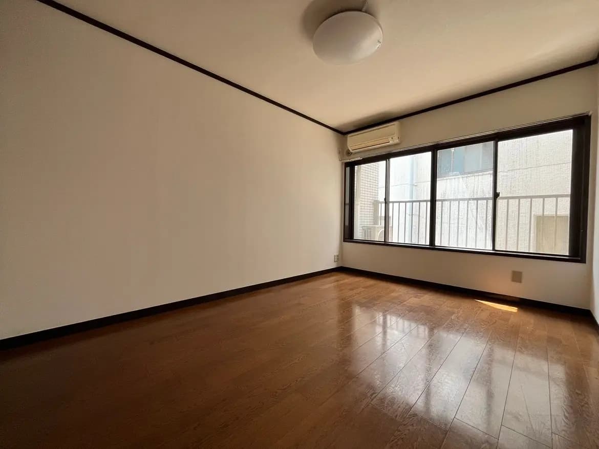 - 照明が明るいシンプルな部屋、木目調のフローリング、大きな窓から外の光が差し込む空間