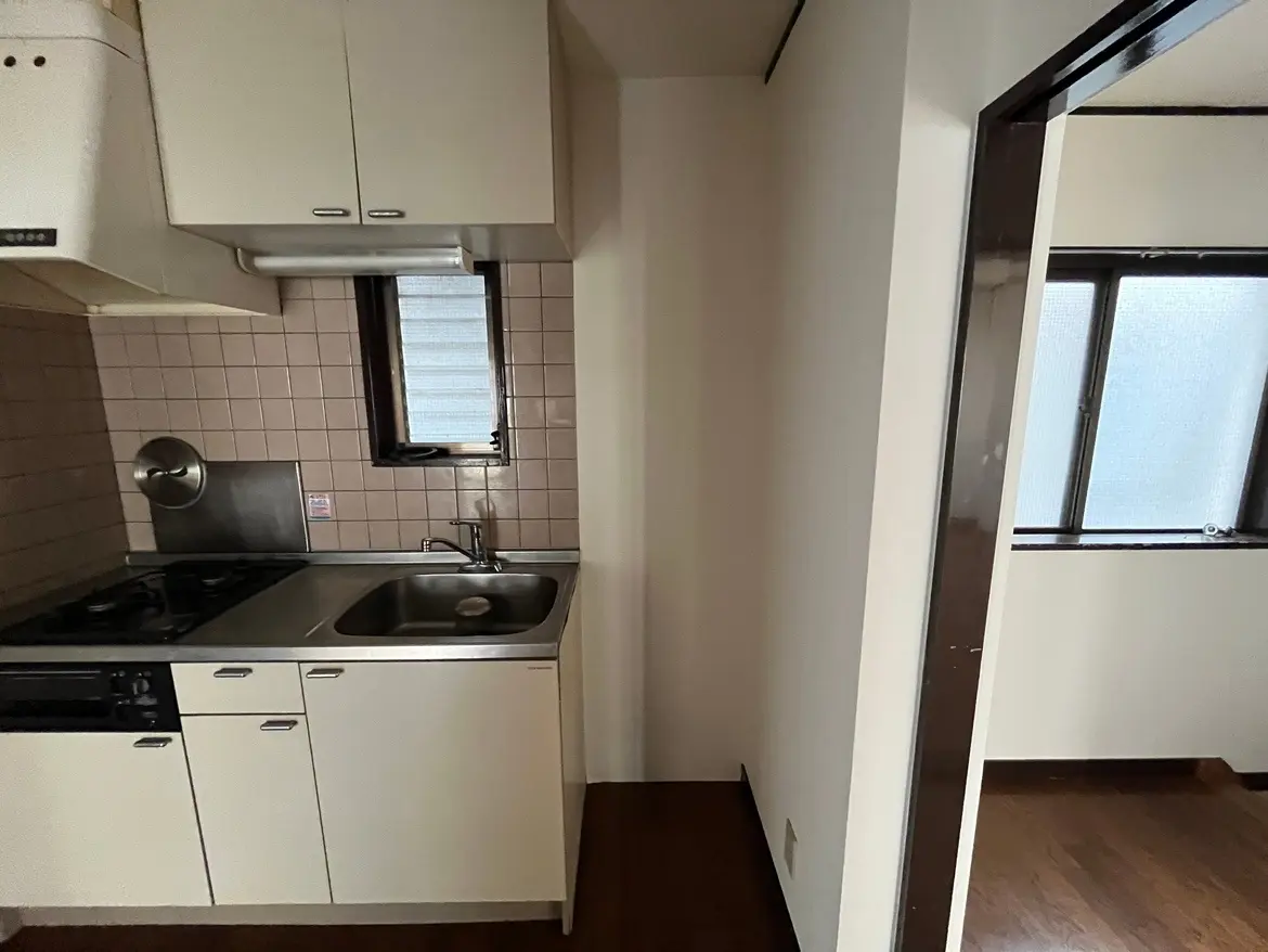 - シンプルなデザインのキッチン、ステンレスのシンクとコンロ、タイル張りの壁があるインテリア、隣接する小窓からの自然光が差し込む様子