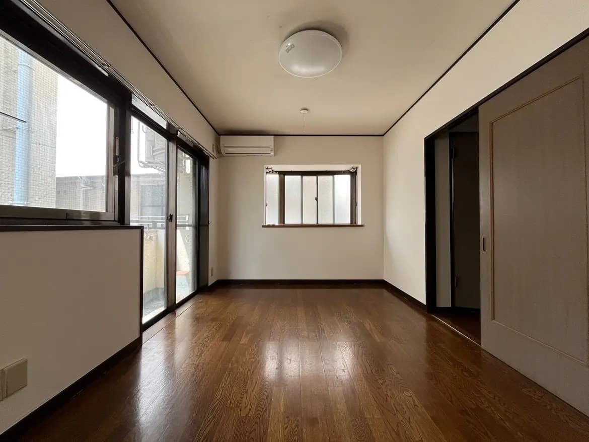 - 明るい木製フローリングの居室、広々とした窓から自然光が入るシンプルなインテリア、エアコン完備の空間