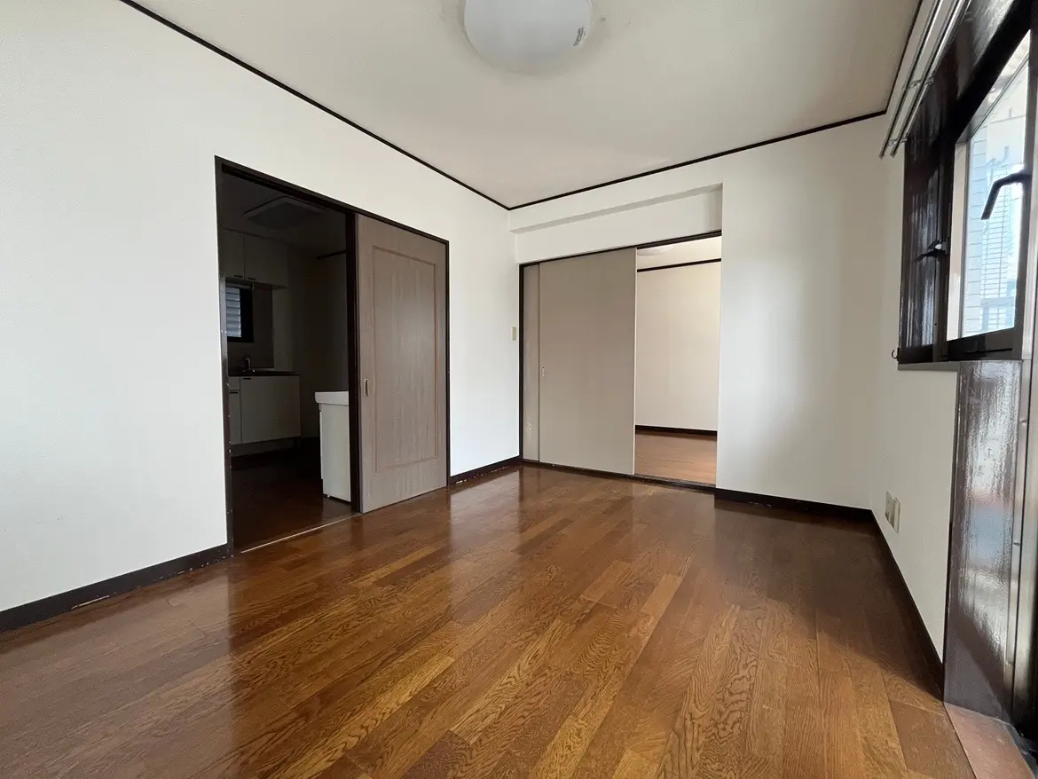 - シンプルな内装のリビングルーム、暖かみのある木製フローリングと隣接するキッチンへのドアがある部屋の写真