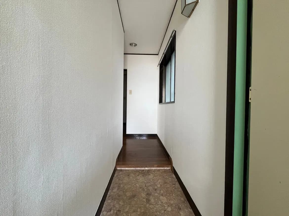 - 明るい壁と木製の床が特徴のシンプルな廊下、左手には窓があり、静かな空間を演出しているインテリア