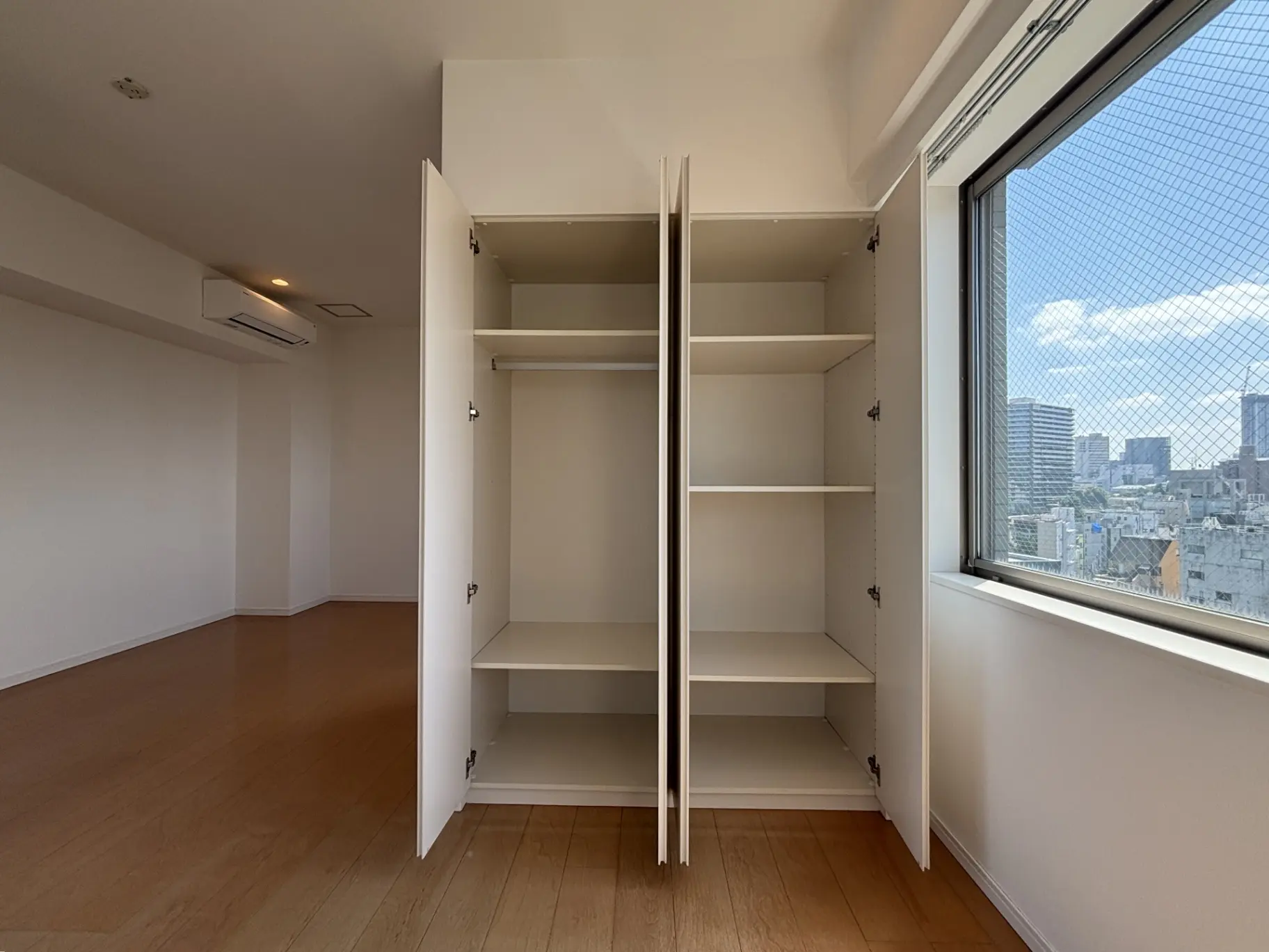 - 明るい部屋の中の大きな収納キャビネット、開いた扉と隣にある窓から見える街の景色