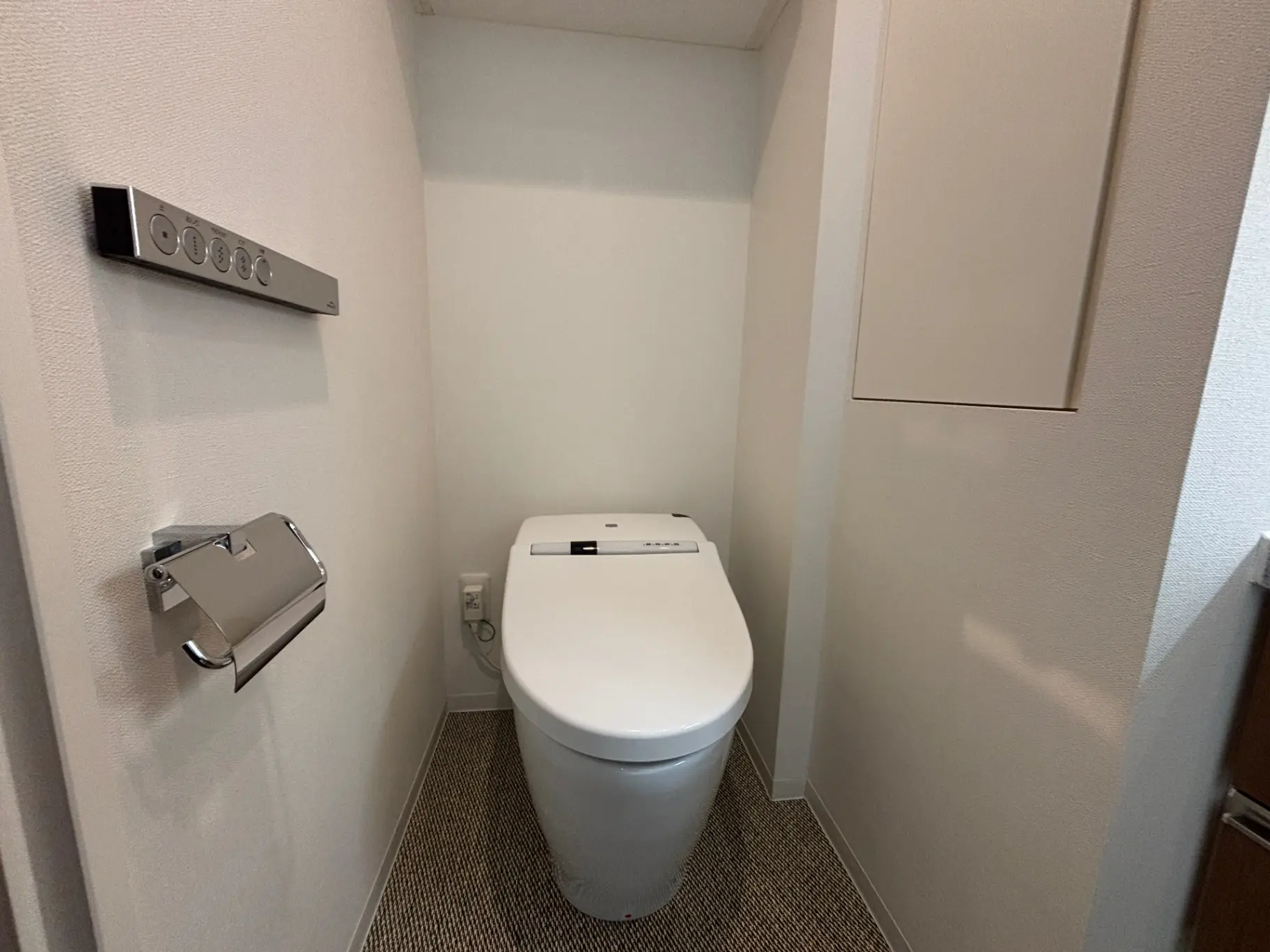- シンプルでモダンなデザインのトイレ、ウォシュレット付き便器、便利な操作パネルとトイレットペーパーホルダーがある空間