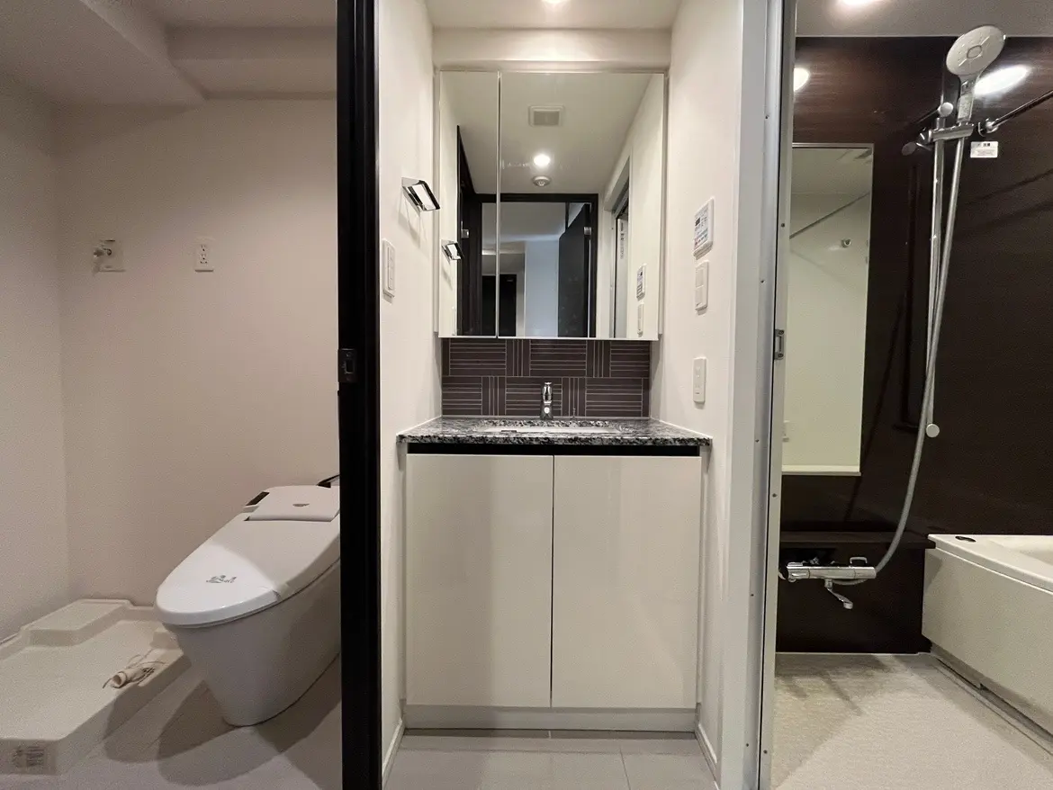 - モダンなデザインのバスルーム、洗面台とトイレが隣接し、シックな色合いのインテリアで統一された空間
