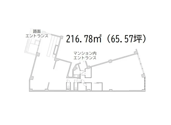 都市の通り沿いに建つモダンな外観の建物、明るい日差しの中、駐車場や看板が見える街角の風景