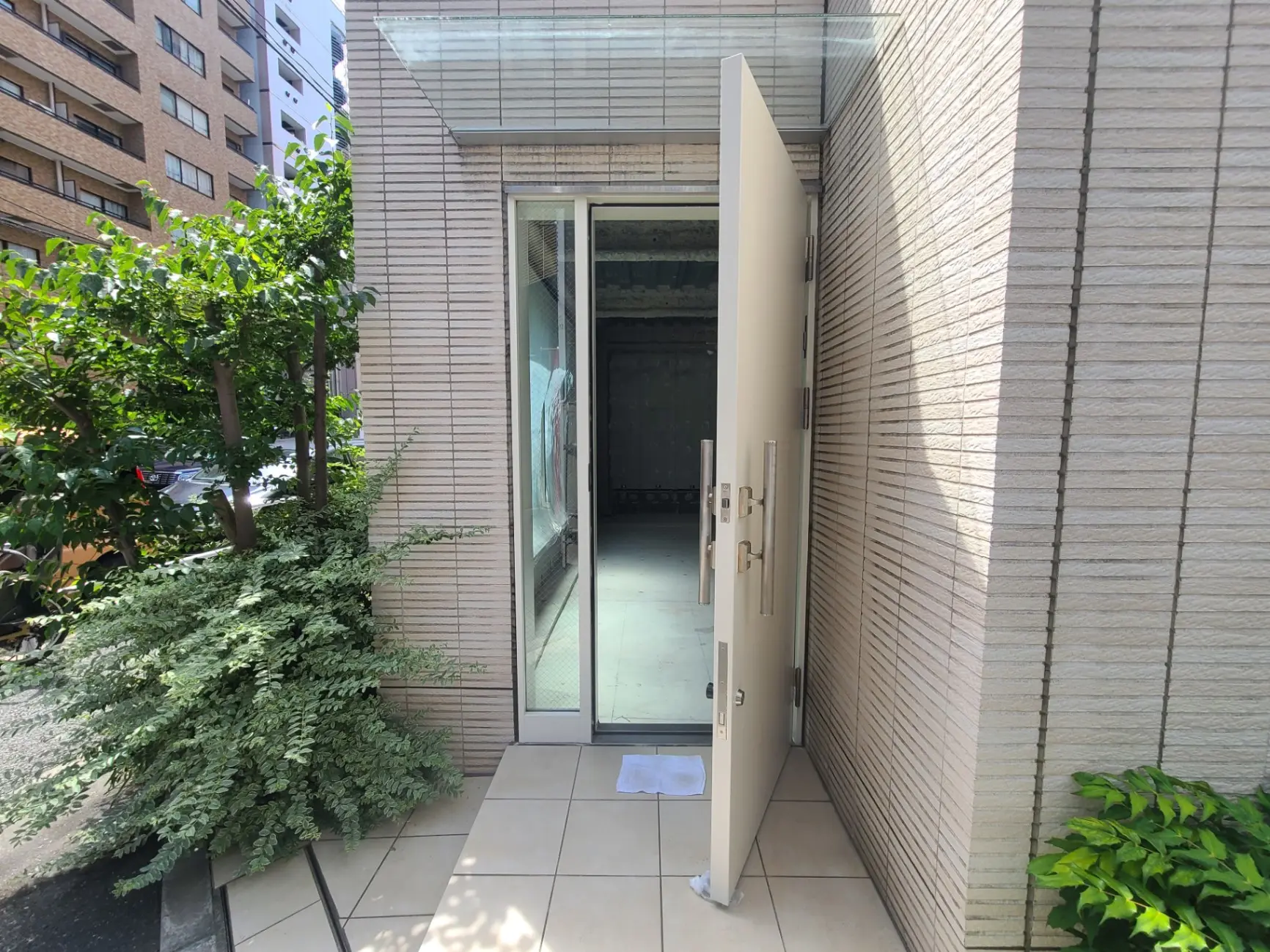 現代的な建物の玄関と外観、開いた扉、緑豊かな植栽と自然光が差し込むエントランス