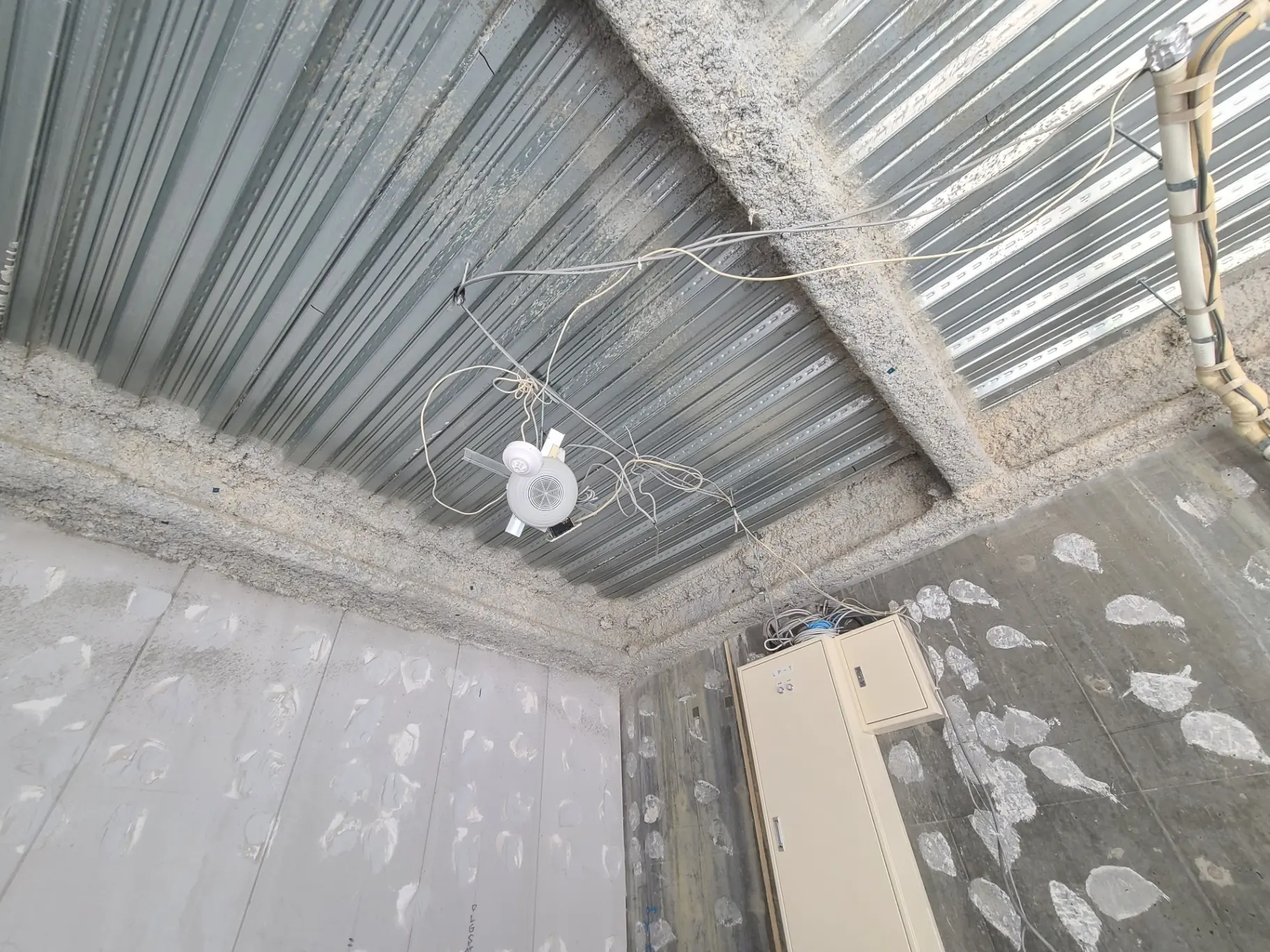 未完成の屋内建築現場、露出した配線と天井ファン、コンクリートの床と壁